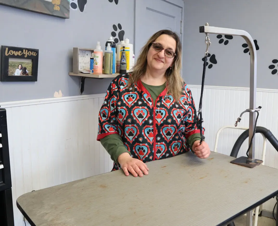 Marina Bagliore behind the grooming table in the salon, wearing a patterned grooming smock